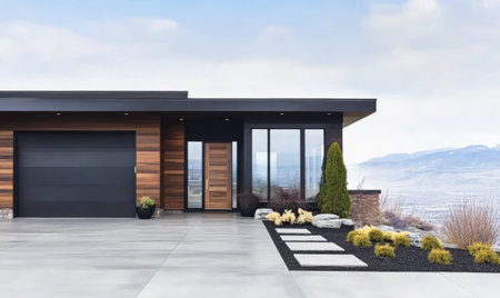 A sleek modern home features a wooden facade and large windows. The front yard is landscaped with shrubs and decorative stones providing an inviting atmosphere against a mountain backdrop.の素材