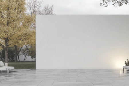 A serene outdoor area with a large, smooth white wall stands out against the backdrop of bare trees displaying autumn foliage. The clean, modern design emphasizes simplicity and tranquility.の素材