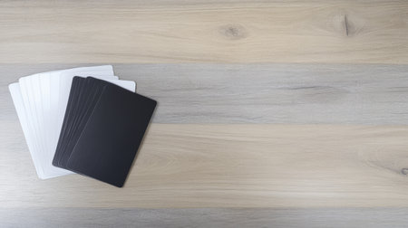 A set of blank white and black cards is neatly arranged on a light wooden surface, suggesting a game or artistic project in progress. The clean layout emphasizes creativity and playfulness.の素材