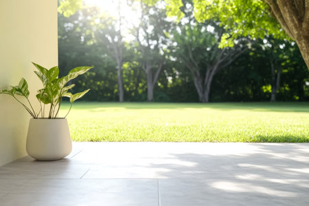 A bright, peaceful outdoor space features a potted plant on a tiled surface, with vibrant green grass and trees in the background. Sunlight filters through the leaves, creating a calming atmosphere.の素材