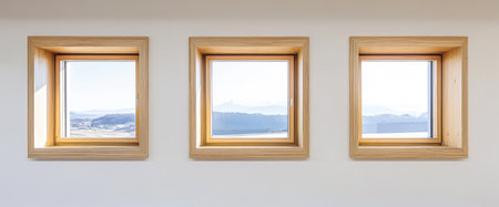 Three wooden-framed windows showcase a tranquil view of distant mountains and green valleys under a clear sky. The light enhances the peaceful surroundings inviting contemplation.の素材