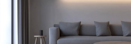 A spacious living room features a stylish gray sofa adorned with pillows. Soft natural light pours in from large windows illuminating the serene interior. A small side table complements the space.の素材