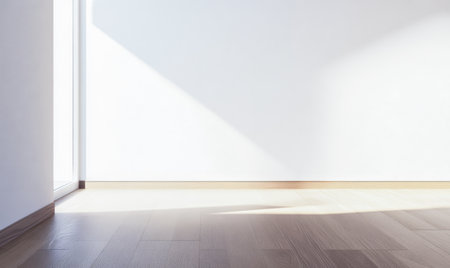 Sunlight streams through a window creating a play of light and shadow on the smooth wooden floor of a simple empty room. The walls are bright enhancing the serene atmosphere.の素材