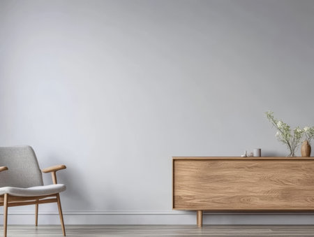 A modern living room showcases minimalistic decor with a light gray wall a wooden sideboard and a cozy chair. A few decorative plants add a touch of nature to the serene atmosphere.の素材