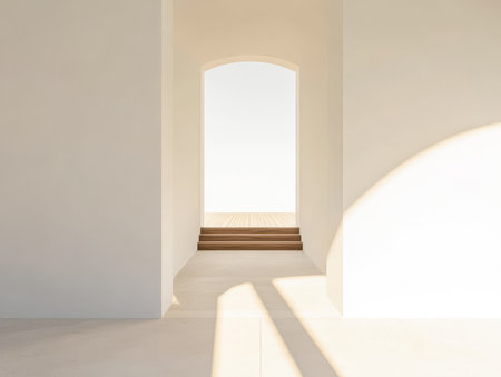 Soft sunlight illuminates a simple hallway with white walls and a wooden staircase. The open doorway frames a serene outdoor vista creating a peaceful atmosphere.の素材