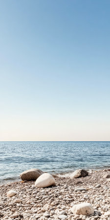 A tranquil shoreline showcases smooth pebbles beside gentle waves lapping at the coast. The serene waters reflect a clear blue sky creating a peaceful atmosphere in nature.の素材