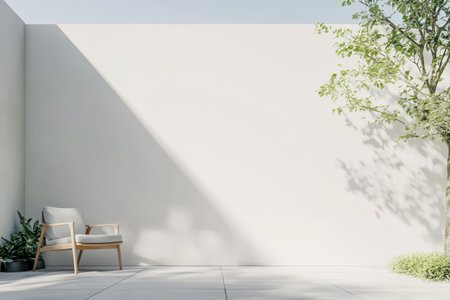A serene outdoor area features a simple wooden chair beside lush plants and a white wall illuminated by bright sunlight. A tree casts soft shadows enhancing the calm atmosphere.の素材