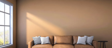 A stylish living room features a comfortable brown leather couch adorned with plush cushions. Soft sunlight streams through a large window illuminating the warm beige walls.の素材