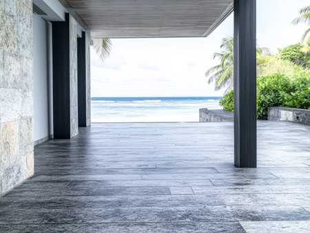 A spacious modern outdoor area showcases elegant stone flooring leading to a breathtaking ocean view surrounded by lush greenery and palm trees under a bright sky.の素材