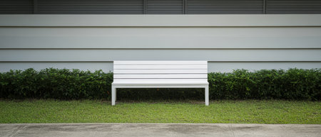 A simple white bench is positioned in a well-kept garden area surrounded by lush greenery and set against a sleek modern white wall. The ambiance is calm and inviting.の素材
