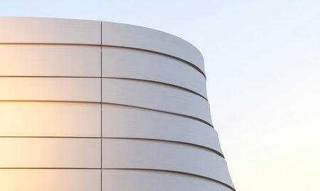 Curved lines of a contemporary building catch the warm glow of the setting sun. The structure showcases innovative design elements against a clear sky adding to the citys landscape.の素材
