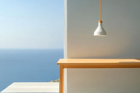 A stylish wooden table stands under a minimalist lamp showcasing a breathtaking view of the calm ocean. The bright atmosphere highlights the tranquility and beauty of the location.の素材