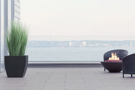 A stylish outdoor balcony featuring a cozy fire pit modern chairs and lush plants under a serene sky. The backdrop reveals a peaceful waterfront and distant cityscape.の素材