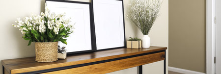 A wooden console table is placed against a neutral wall featuring two empty picture frames and decorative vases. Lush greenery and minimalist decor create a harmonious atmosphere in the room.の素材