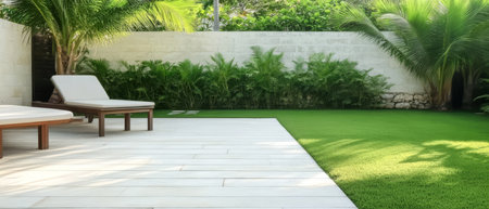 Two modern loungers rest on a wooden deck under the sun framed by vibrant green plants and a well-maintained lawn creating an inviting outdoor space for relaxation.の素材
