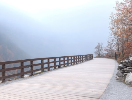 A serene wooden walkway meanders through a foggy forest surrounded by trees with autumn foliage. The atmosphere is calm and quiet evoking a sense of peace at dawn.の素材