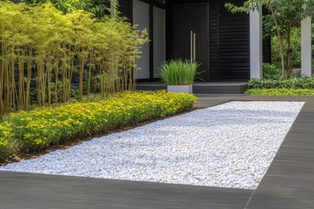 A contemporary garden showcases a clean white gravel path bordered by lush yellow flowers and green grass. The design emphasizes simplicity and natural beauty under clear skies.の素材