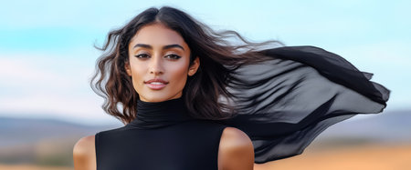 A model stands gracefully outdoors with flowing hair and a lightweight black garment that billows in the wind.の素材