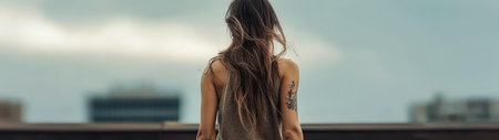 A young woman stands on a rooftop her long hair flowing in the breeze as she gazes at the skyline of the city at twilight. The atmosphere is calm and reflective with building silhouettes.の素材
