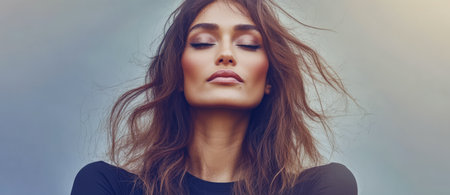 A woman stands with her eyes closed embracing the moment as her hair flows in the breeze. The lighting creates a soft and warm atmosphere highlighting her serene expression.の素材