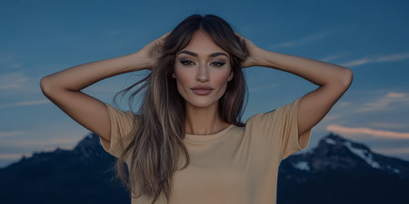 A confident woman stands with her hands in her hair showcasing a serene expression. She is surrounded by towering mountains under a colorful twilight sky evoking a sense of tranquility and freedom.の素材