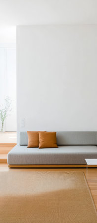 A spacious living room featuring a pale gray couch adorned with two brown cushions. The wooden floor and large windows allow plenty of natural light enhancing the airy atmosphere.の素材