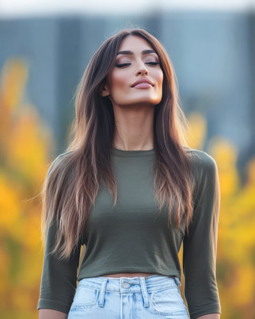 A young woman with long flowing hair stands calmly in an outdoor environment. She wears a fitted green top and high-waisted jeans.の素材