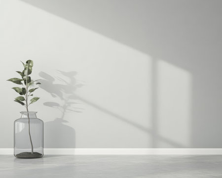 A single green plant in a clear glass vase sits against a light grey wall casting a long shadow. The sunlight creates a calm and inviting atmosphere in the minimalist space.の素材