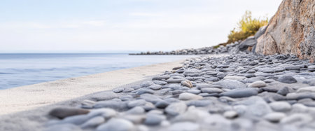 A picturesque pebble beach stretches along the shoreline with smooth stones glistening under the sunlight. The calm ocean reflects a tranquil sky enhancing the peaceful atmosphere.の素材