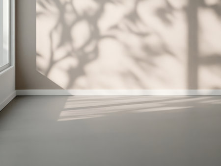 Bright sunlight filters through a window creating intricate shadows on a plain wall. The light enhances the minimalist decor emphasizing the softness of the space and shadows.の素材
