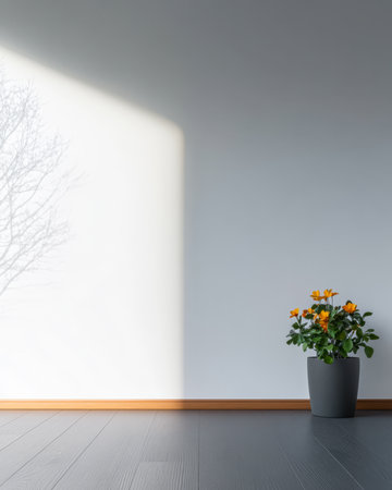 A minimalist indoor space features a potted plant with vibrant yellow flowers placed against a light-colored wall. Natural sunlight casts soft shadows enhancing the tranquility of the room.の素材
