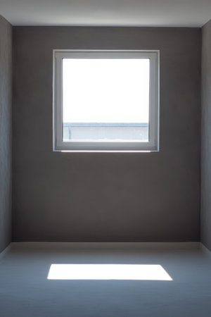 A minimalistic gray room features a window that allows bright daylight to illuminate the space. The simplicity of the design emphasizes tranquility and openness creating a serene atmosphere.の素材