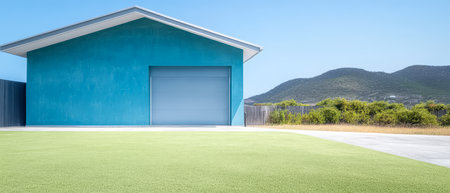A modern blue structure features a spacious opening surrounded by vibrant green grass and rolling hills in the background. Clear blue skies enhance the tranquil setting during daylight.の素材