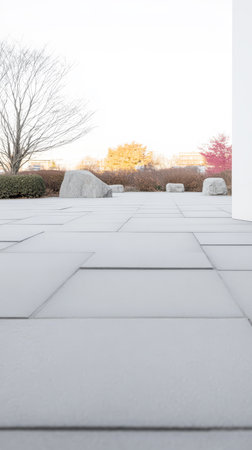 A serene outdoor setting with smooth light-colored paving stones scattered natural rocks and sparse greenery. Trees bare of leaves contrast with the bright sky creating a calming atmosphere.の素材