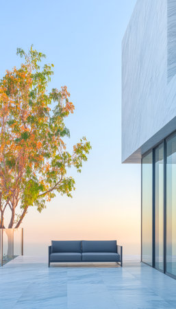 A sleek outdoor area features a contemporary couch positioned against a glass wall. A colorful tree stands nearby bathed in the warm glow of the sunset atmosphere.の素材