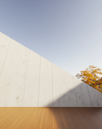A tilted concrete wall rises against a bright blue sky with warm wooden flooring visible in the foreground. An autumn tree with vibrant leaves adds a touch of color to the serene setting.の素材