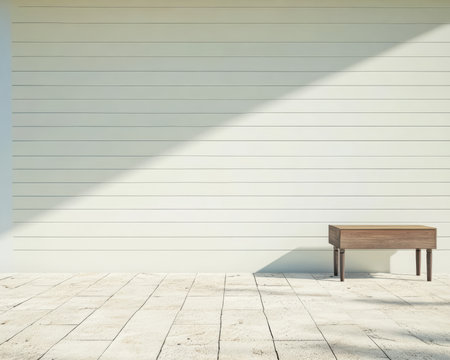 A wooden table with tapered legs sits quietly against a light-colored lined wall illuminated by natural sunlight on a stone patio. The atmosphere is calm and serene.の素材