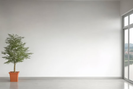 Bright indoor area showcases a single potted tree beside a large window illuminating the minimalist design. The walls are bare emphasizing a calm and spacious atmosphere.の素材