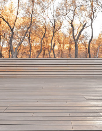 A modern wooden deck showcases clean lines and a spacious area surrounded by tall trees with warm autumn colors. The golden hour sunlight enhances the serene atmosphere creating a tranquil setting.の素材