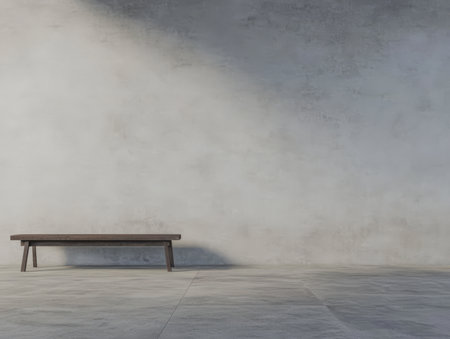 A simple wooden bench stands alone in a minimalist interior. The plain grey wall contrasts with the bench highlighting the clean lines of contemporary design. The lighting adds depth.の素材