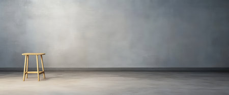 A single wooden stool sits in an empty modern room with a smooth gray wall and floor. The minimalist design emphasizes the simplicity of the setting creating a serene atmosphere.の素材