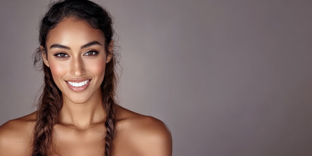 A woman with long braided hair is smiling brightly showcasing her confidence and joy. The soft neutral background enhances her features creating an inviting atmosphere.の素材