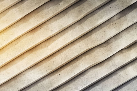 Diagonal grooves create a dynamic texture on the concrete wall highlighted by soft daylight. The design emphasizes rhythm and depth enhancing the visual appeal of the surface.の素材