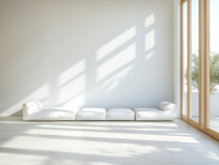 A bright and airy room features a long white sofa positioned against a light wall. Sunlight streams through large windows casting soft shadows on the floor.の素材