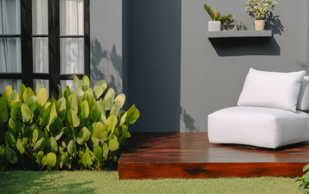 A cozy outdoor seating area features a stylish white lounge chair adjacent to lush green plants. Sunlight filters through enhancing the serene atmosphere in this inviting space.の素材