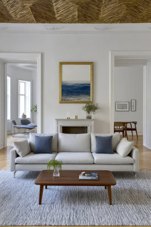 A modern living room showcases a stylish sofa with blue cushions a wooden coffee table and a decorative painting.の素材