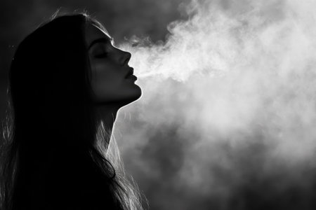 A woman with long hair is silhouetted against a dark background, exhaling a cloud of smoke. The atmosphere is moody and evokes a sense of mystery and calm.の素材