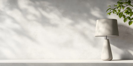 A modern desk displays a chic lamp beside a light wall, where soft shadows from nearby foliage create a tranquil atmosphere. Natural light enhances the serene vibe of the setting.の素材