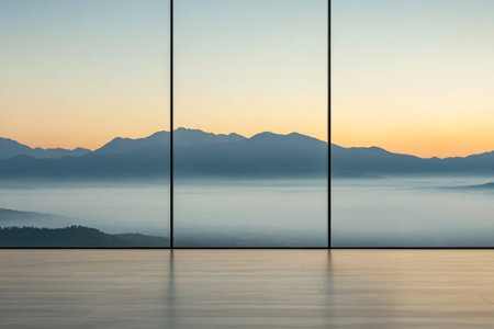 A stunning view of distant mountains illuminated by the soft glow of sunrise. The scene captures mist rolling through the valleys beneath clear skies from within a contemporary space.の素材