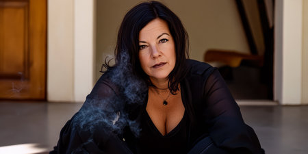 A woman sits calmly on the floor, gazing intently with a serene expression. Smoke wafts around her, highlighting a stylish indoor environment. Her attire exudes elegance and confidence.の素材